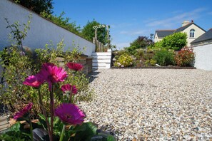 A gravel driveway leading to a house with a white wall and a wooden fence.