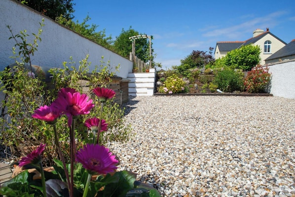 A gravel driveway leading to a house with a white wall and a wooden fence.