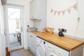 A compact kitchen with a washing machine, wooden countertop, and a small wooden drying rack.