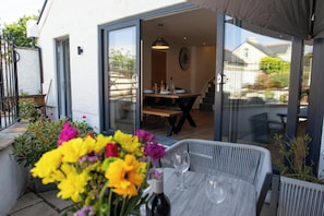 An outdoor dining area with a table and chairs, a glass door leading to an interior dining room, and a variety of potted plants.