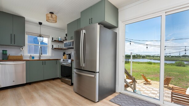 Eine moderne Küche mit einem Edelstahlkühlschrank, grünen Schränken und einer großen Schiebeglastür, die auf eine Terrasse mit Sitzgelegenheit führt.