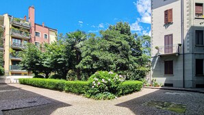 A courtyard with a gravel path, green hedges, and a flower bed with pink flowers.
