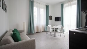A modern living room with a sofa, dining table, and kitchen area.