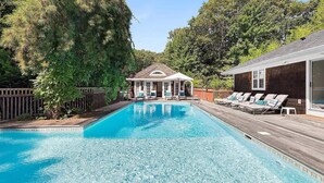 Et rektangulært swimmingpool med en træterrasse og liggestole på den ene side.
