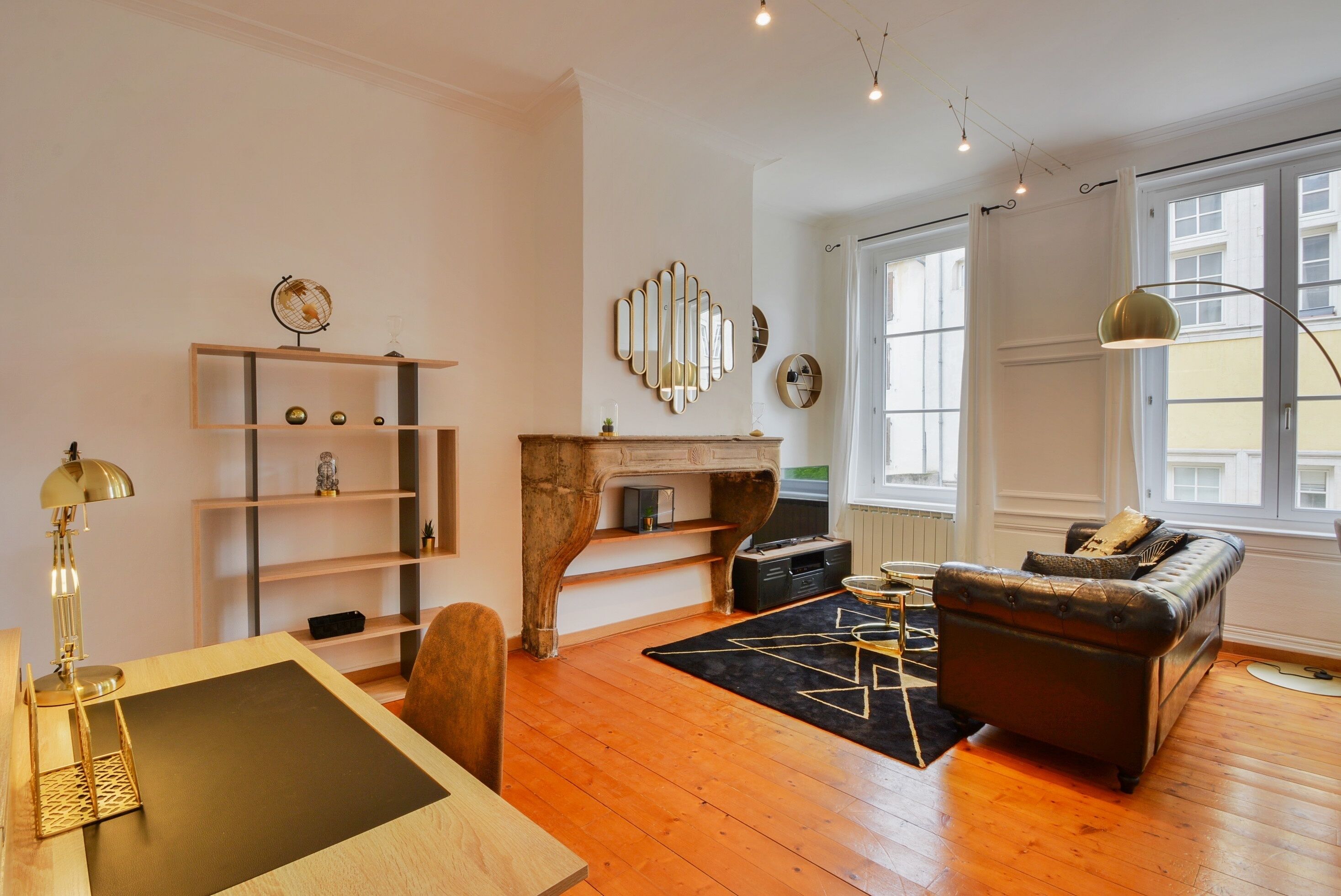 A living room with a wooden floor, a leather sofa, a coffee table, a fireplace, shelves, and a lamp.