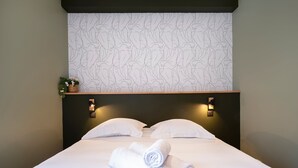 A neatly made bed with two pillows and two rolled towels, a wall with a leaf pattern, and two wall-mounted light fixtures. - La Cachette de Stanislas - Centre-ville de Nancy (Nancy)