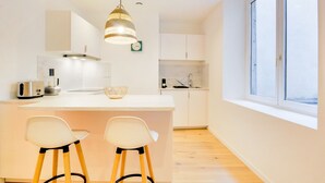 A modern kitchen with a central island, two bar stools, a hanging light fixture, and a large window. - Le Cachet de la Craffe - Au cœur de Nancy (Nancy)