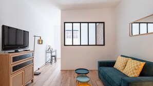 A modern living room with a flat-screen TV, wooden cabinet, multi-colored side tables, and a green sofa with patterned cushions. - L'Alerion Nancéien - Charme au coeur de Nancy (Nancy)