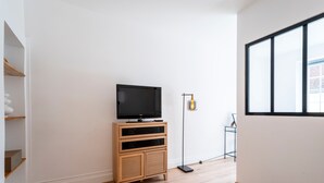 A modern living room with a flat-screen TV on a wooden cabinet, a floor lamp, and a large window. - L'Alerion Nancéien - Charme au coeur de Nancy (Nancy)