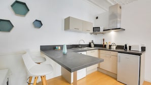 A modern kitchen with a central island, white cabinets, a built-in microwave, and a compact refrigerator. - Le Cocon des Ponts - Studio 29 m² à Nancy (Nancy)