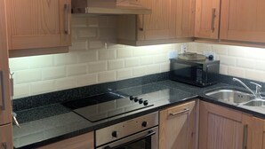 A kitchen with wooden cabinets, a black countertop, a stainless steel oven, and a microwave. - Delightful Howth Village apartment in Dublin (Dublin)
