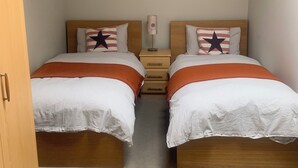 A bedroom with two beds, each with a wooden headboard, a nightstand, and a lamp between the beds. - Delightful Howth Village apartment in Dublin (Dublin)