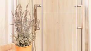 A shower with a glass door, a wooden panel wall, and a potted plant on a shelf.