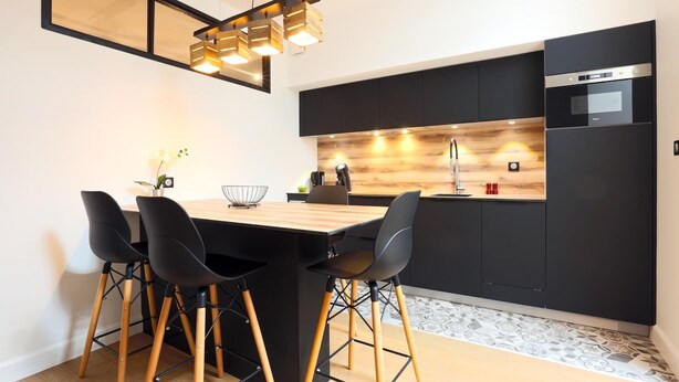 Une cuisine moderne avec une table à manger en bois, des chaises noires et un four encastré.