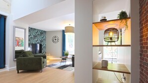 Un salon moderne avec un canapé vert, un téléviseur à écran plat et un mur décoré d’un motif.