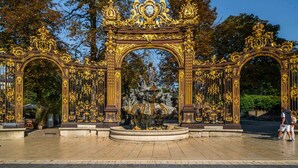 An ornate golden archway with a central fountain, surrounded by trees.