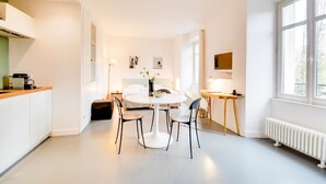 A modern, well-lit room with a round dining table, chairs, a small side table, and a bed with a white headboard. - L'Hôtel Particulier - L'appartement de Nicole (Nancy)