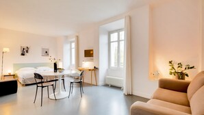 A modern hotel room with a bed, a dining area with a table and chairs, a sofa, and a large window with curtains. - L'Hôtel Particulier - L'appartement de Nicole (Nancy)