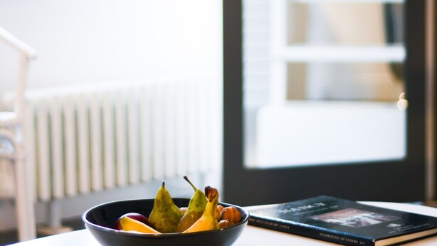 A bowl of fruit on a table with a book beside it, near a window with a view of a bookshelf and a plant. - L'Hôtel Particulier - L'appartement de Pierre (Nancy)