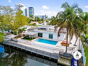 A modern house with a swimming pool, a covered patio, and a dock extending into a body of water. - Uhost AI Miami 5BR Heated Pool Hot Tub (Aventura)