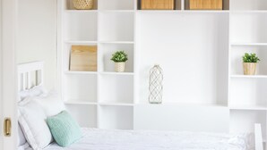 Una habitación blanca con una cama, un armario blanco con estantes y una puerta.