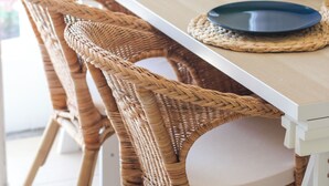 Un comedor con una mesa blanca, sillas de mimbre y una pequeña planta en maceta.