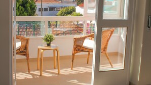 Un balcón con sillas de mimbre y una mesita, con vistas a una zona costera con edificios y árboles.