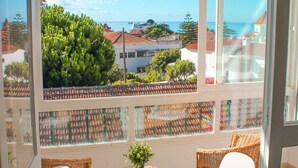 Un balcón con sillas de mimbre y una mesa pequeña, con vistas a un pueblo costero con casas y árboles.