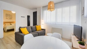 A modern living room with a grey sofa, white chairs, a round table, a TV, and a large window with sheer curtains. - L'indépendant de la rue du Tapis Vert - Appt Nancy (Nancy)