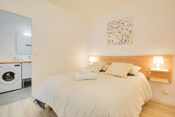 A bedroom with a bed, a washing machine, and a wall-mounted artwork. - L'indépendant de la rue du Tapis Vert - Appt Nancy (Nancy)