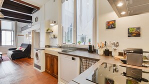 A compact kitchen with a dishwasher, a coffee machine, and a microwave. There is a window with sheer curtains and a small balcony with a chair. - Le cocon des Deux Sirènes - Studio cosy pour 2 à Nancy (Nancy)