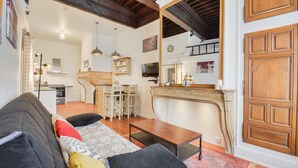 A living room with a sofa, a coffee table, and a fireplace. There is a dining area with a table and chairs in the background. - Le cocon des Deux Sirènes - Studio cosy pour 2 à Nancy (Nancy)