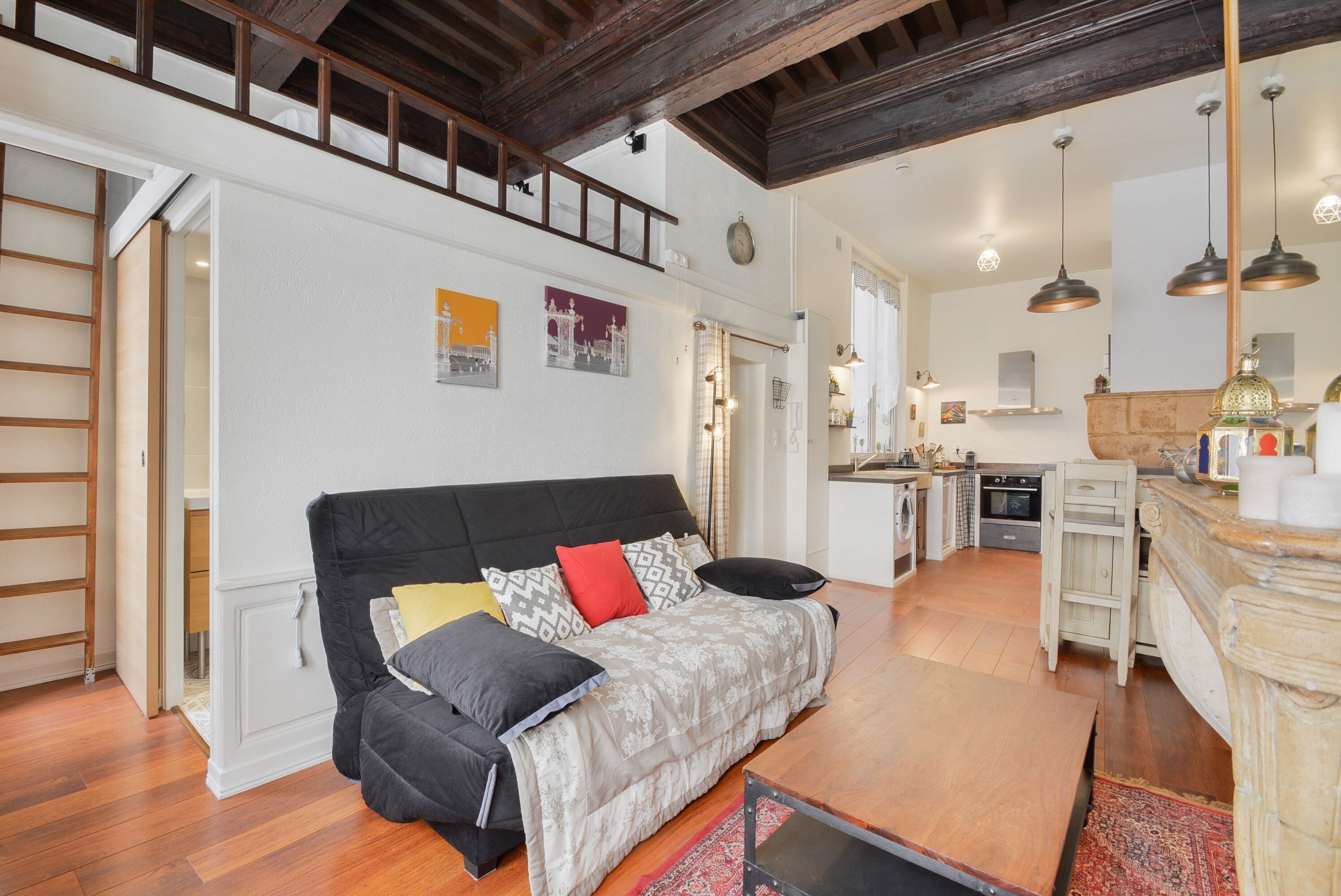 A cozy living room with a black sofa, a wooden coffee table, and a kitchen area in the background.