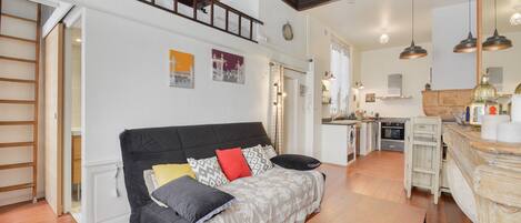 A cozy living room with a black sofa, a wooden coffee table, and a kitchen area in the background.