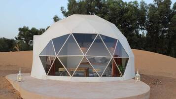 Une structure en forme de dôme géodésique, avec un lit central et une petite table, le tout entouré d’une plateforme circulaire.