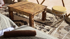 A wooden table with intricate carvings, accompanied by two stools with cushioned seats, set on a patterned rug. - Merzouga dome  (Rissani)