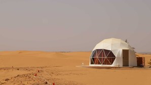 A dome-shaped building in a desert with a flat roof and large windows. - Merzouga dome  (Rissani)