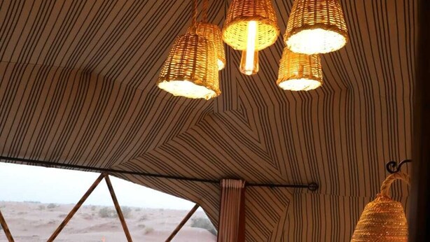 A cozy, striped-patterned tent with a bed, a small table, and hanging lamps. - Merzouga dome  (Rissani)