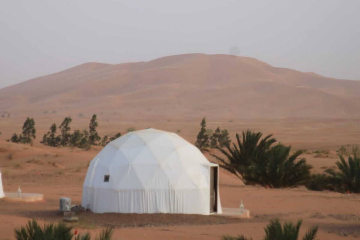 A dome-shaped structure in a desert landscape with a mountain in the background.