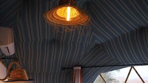 A cozy, striped tent-style room with a bed, pillows, a hanging light fixture, and a view of the desert outside. - Merzouga dome  (Rissani)