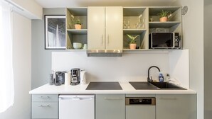 A modern kitchen with white cabinets, a built-in microwave, a coffee station, and a sink. - Le Coquet de Simon - Proche de la place Stanislas (Nancy)