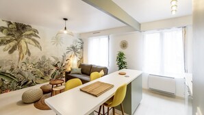 A modern living room with a white sofa, yellow chairs, a dining table, and a large tropical mural on the wall. - Le Coquet de Simon - Proche de la place Stanislas (Nancy)