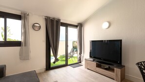 Ein modernes Wohnzimmer mit einem Flachbildfernseher, einer Couch, einem Couchtisch und einer Glastür, die auf einen Balkon mit Gartenmöbeln führt.