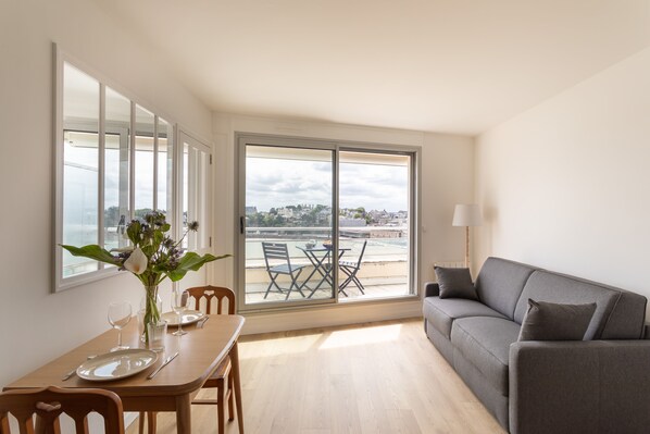 Un comedor con una mesa preparada para dos, un sofá y vistas de la ciudad a través de amplias ventanas.
