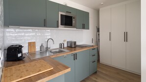 A modern kitchen with teal cabinets, a stainless steel microwave, a sink, and a wooden countertop. - L'Escale Panoramique - Appt vue mer à Dinard (Dinard)