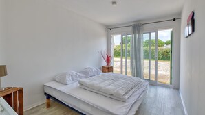 Une chambre à coucher avec un lit, une table de chevet, une fenêtre avec des rideaux et une vue sur la verdure à l’extérieur.