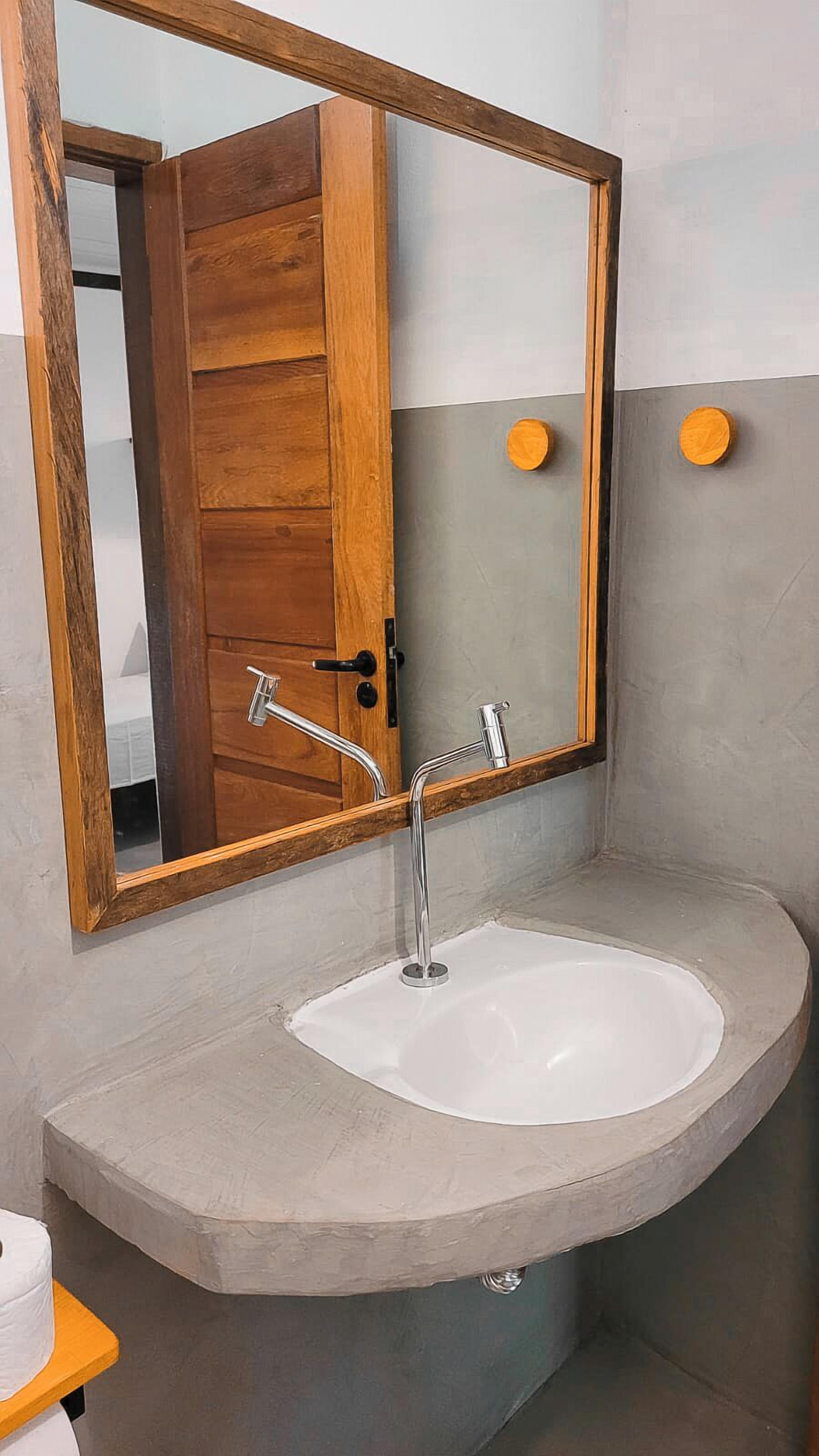 Ein Badezimmer mit Holztür, Waschbecken in Weiß und einem Spiegel mit Holzrahmen.