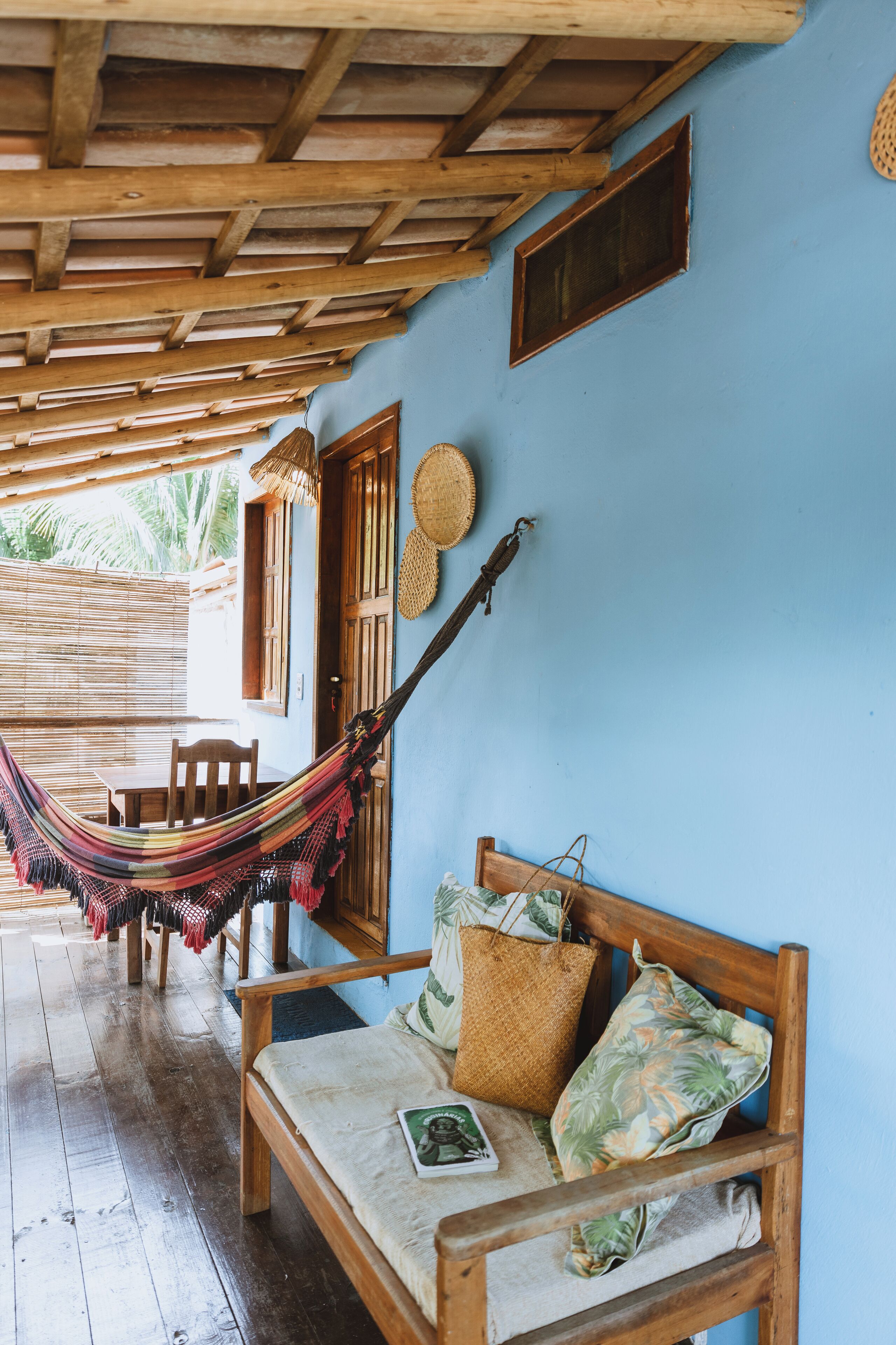 Un banc en bois avec un hamac tressé, une table en bois et un mur bleu avec une porte en bois et une fenêtre.