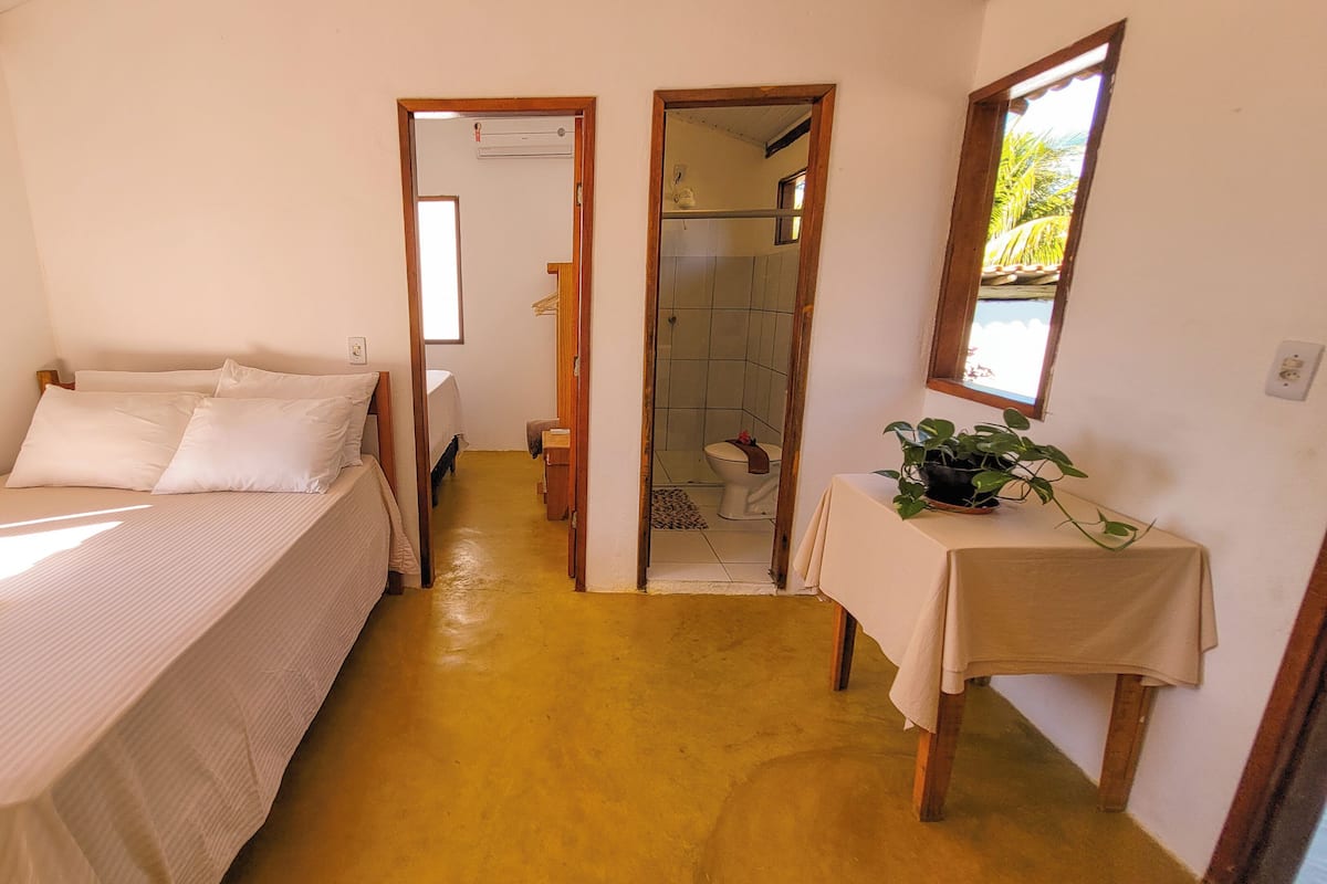 A bedroom with a bed, a bedside table with a plant, and a bathroom visible through an open door.