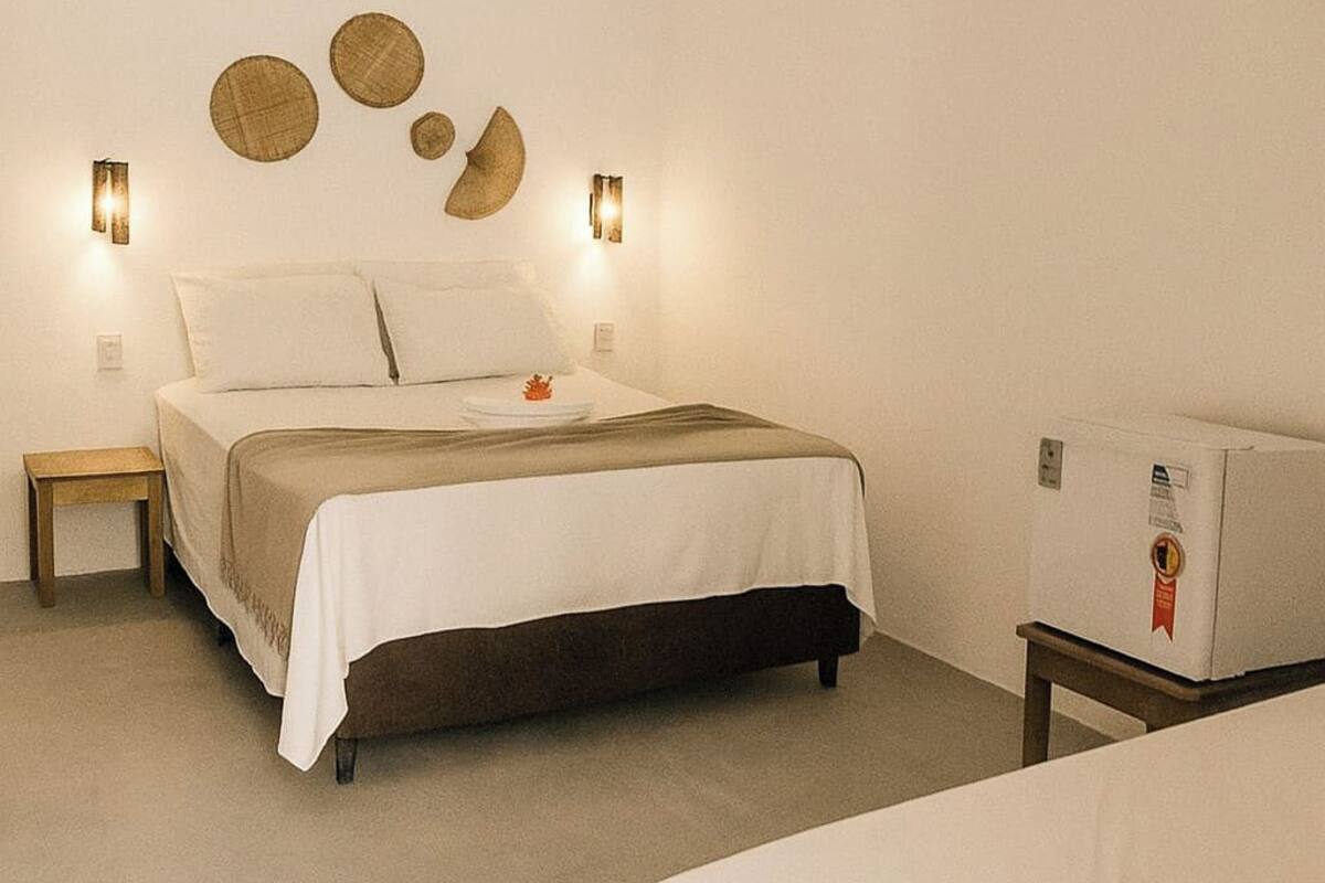 A hotel room with a bed, bedside tables, wall-mounted lights, and an air conditioning unit.